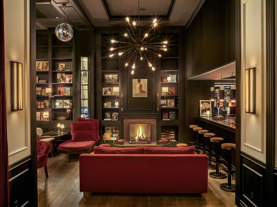 A cozy lounge area with a fireplace, red seating, and a bar with stools.