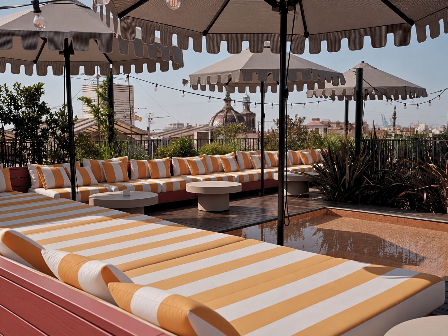 Eine Dachterrasse mit gestreiften Liegestühlen und Hocker, umgeben von Sonnenschirmen und Lichterketten.