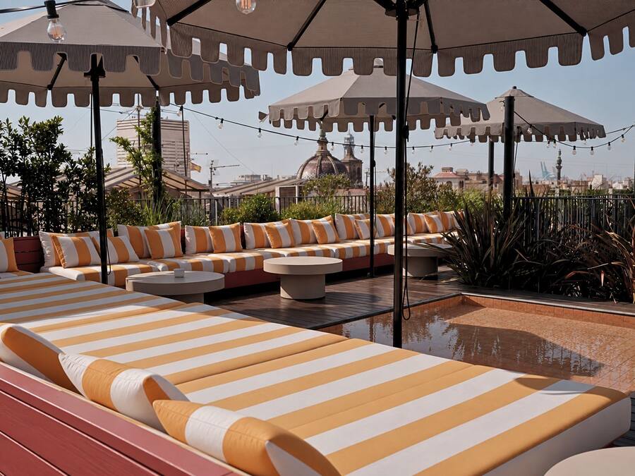 A rooftop lounge area with striped lounge chairs and ottomans, surrounded by umbrellas and string lights.