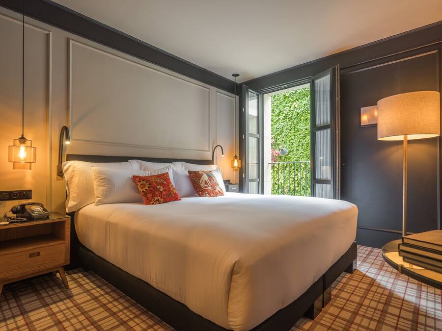 Habitación de hotel con una cama grande, una mesita de noche con teléfono, una lámpara y vistas a zonas verdes.