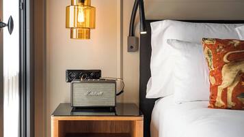 A neatly made bed with a white pillow and a decorative pillow with a dog design. A vintage radio is placed on a wooden nightstand beside the bed. A modern pendant light hangs above the radio.