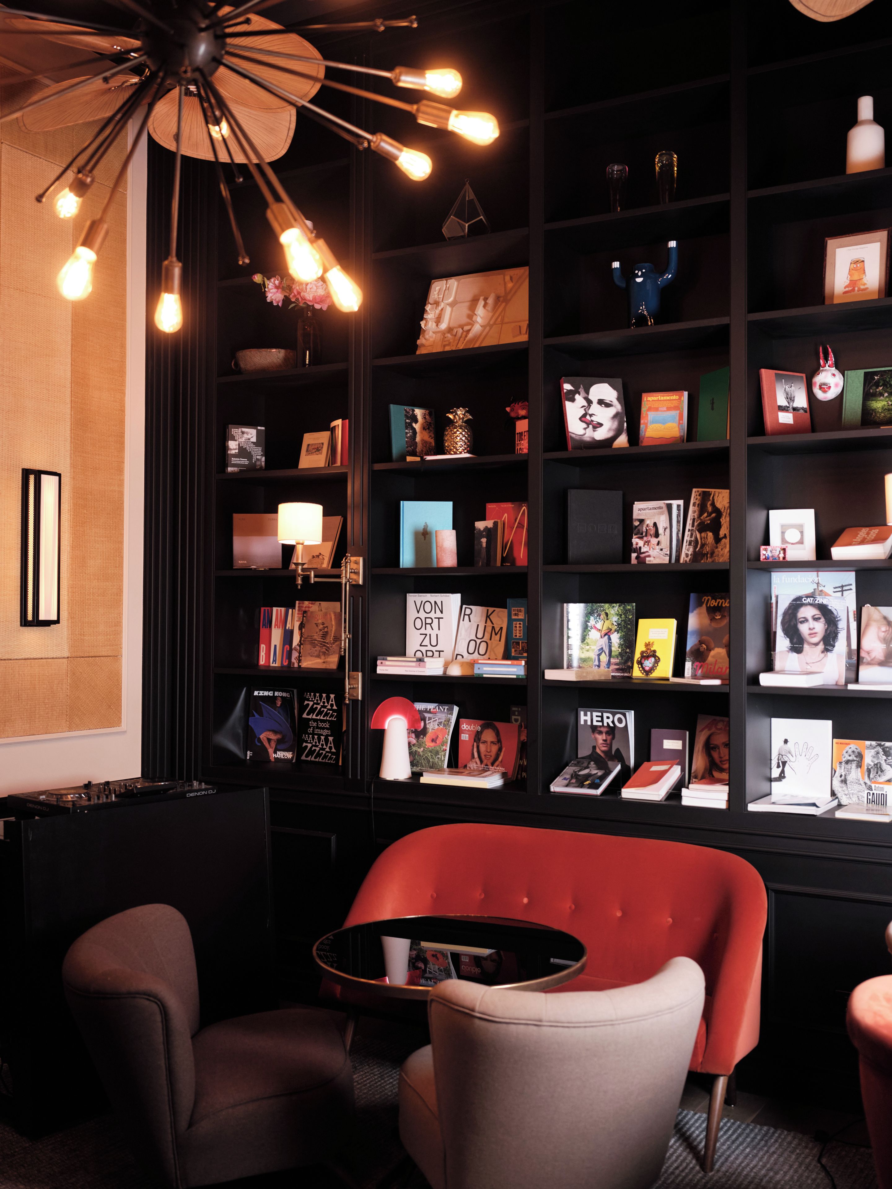 A modern interior with a black bookshelf, a red armchair, and a DJ setup.