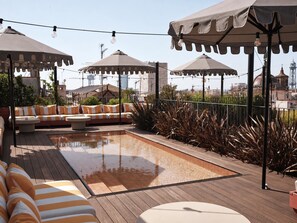 Un espace extérieur aménagé avec des sièges, une piscine, des parasols et une vue sur le paysage urbain.