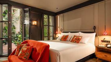 A modern hotel room with a large bed, a red armchair, and a view of greenery through the windows.