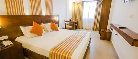 A hotel room with a large bed, a desk, a chair, a TV, and curtains.