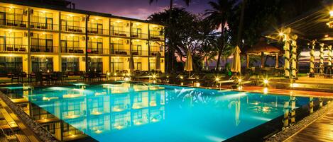 A hotel with a swimming pool, multiple balconies, and outdoor seating areas.