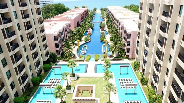 Un hôtel de grande hauteur doté de plusieurs piscines, de palmiers et offrant une vue sur la mer.