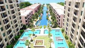 A high-rise hotel with multiple swimming pools, palm trees, and a view of the sea. - Marrakesh Condo Residence by Hua hin property online (Hua Hin)