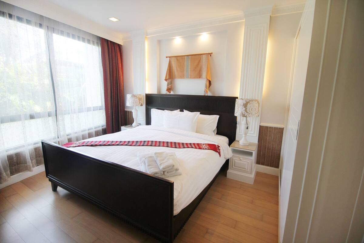 A neatly made bed with white linens and a red and white striped blanket, a wooden headboard, and a bedside table with a lamp.