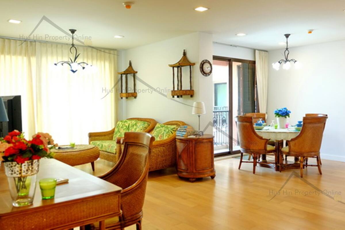 A spacious living room with a dining area, wooden furniture, and a balcony with a view.