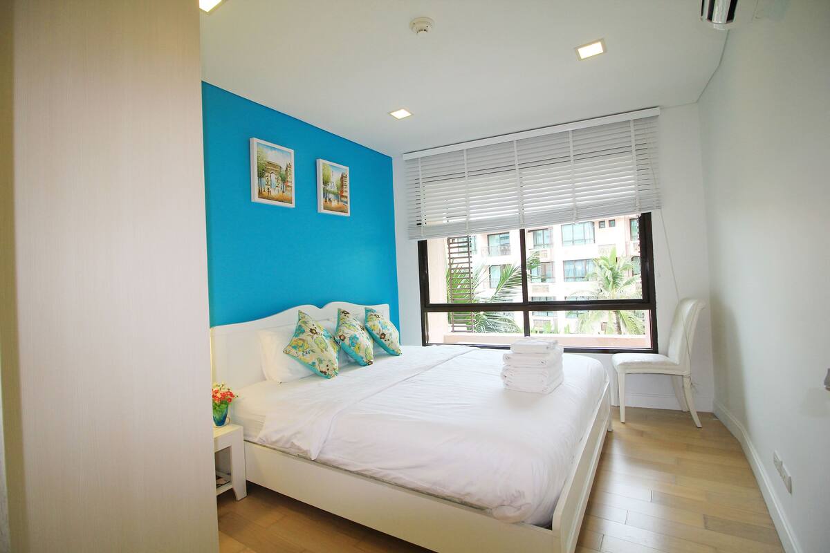 A bedroom with a bed, a nightstand, a chair, and a window with blinds.
