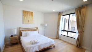 Une chambre d’hôtel bien rangée, avec un grand lit, une table de chevet avec une lampe, une fenêtre avec des rideaux et un tableau accroché au mur.