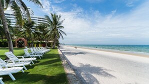 Une plage avec des chaises longues blanches alignées sur l’herbe, un ciel bleu dégagé et l’océan en arrière-plan.