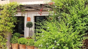 Un edificio de dos pisos con un balcón, plantas en macetas y una puerta de madera.