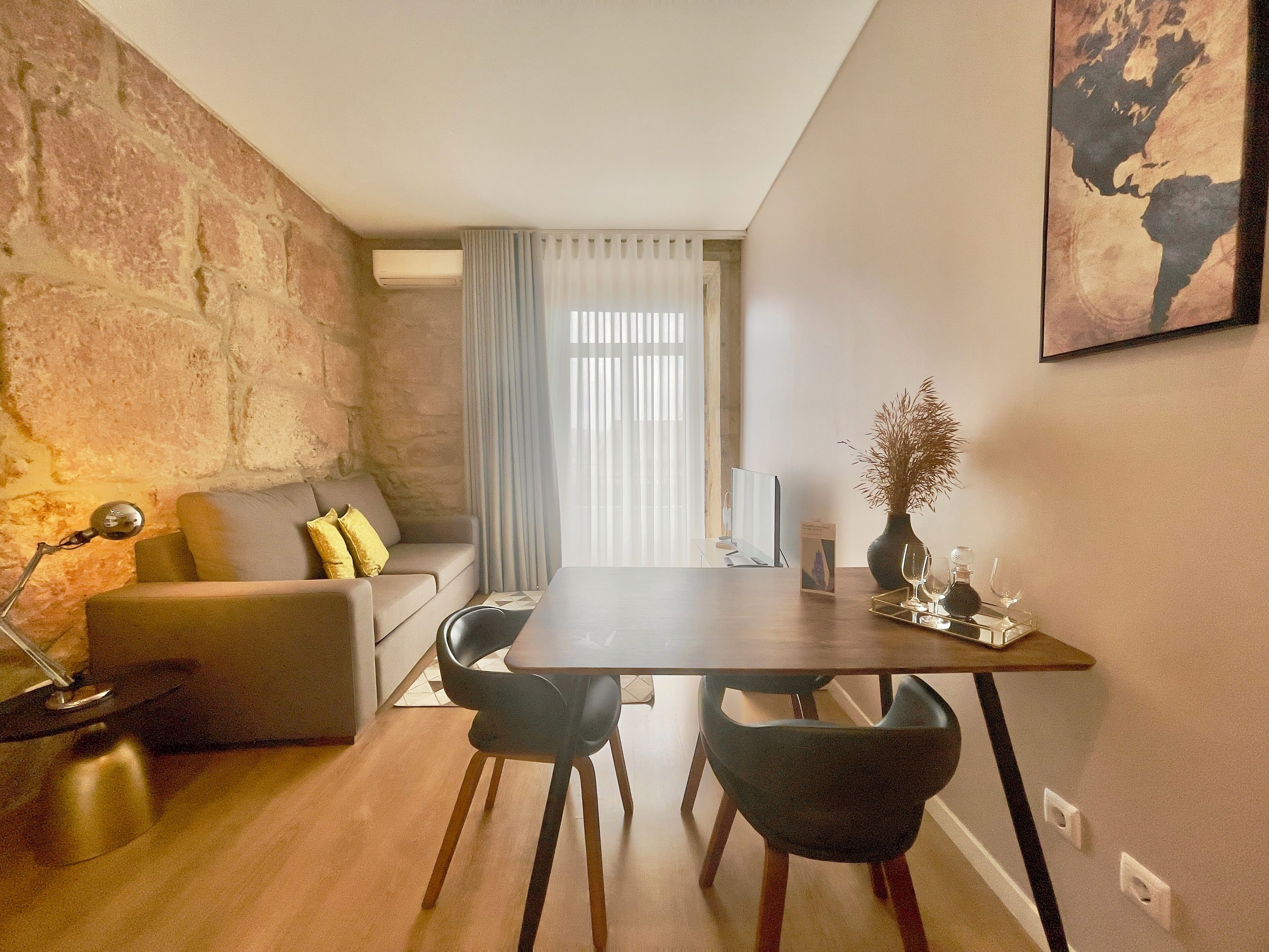 A cozy living area with a sofa, a dining table, and chairs. There is a lamp, a vase with flowers, and a framed picture on the wall.