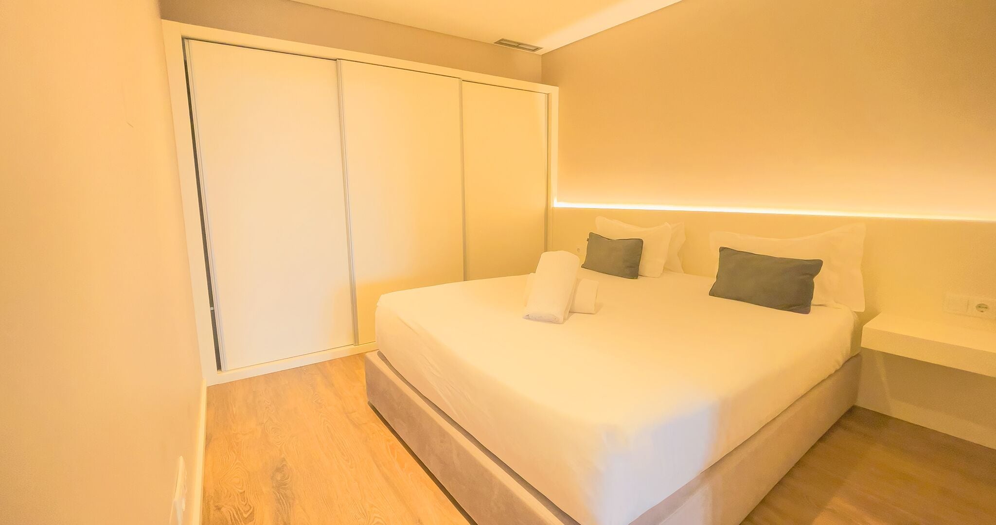A bedroom with a bed, pillows, a nightstand, and a wardrobe.