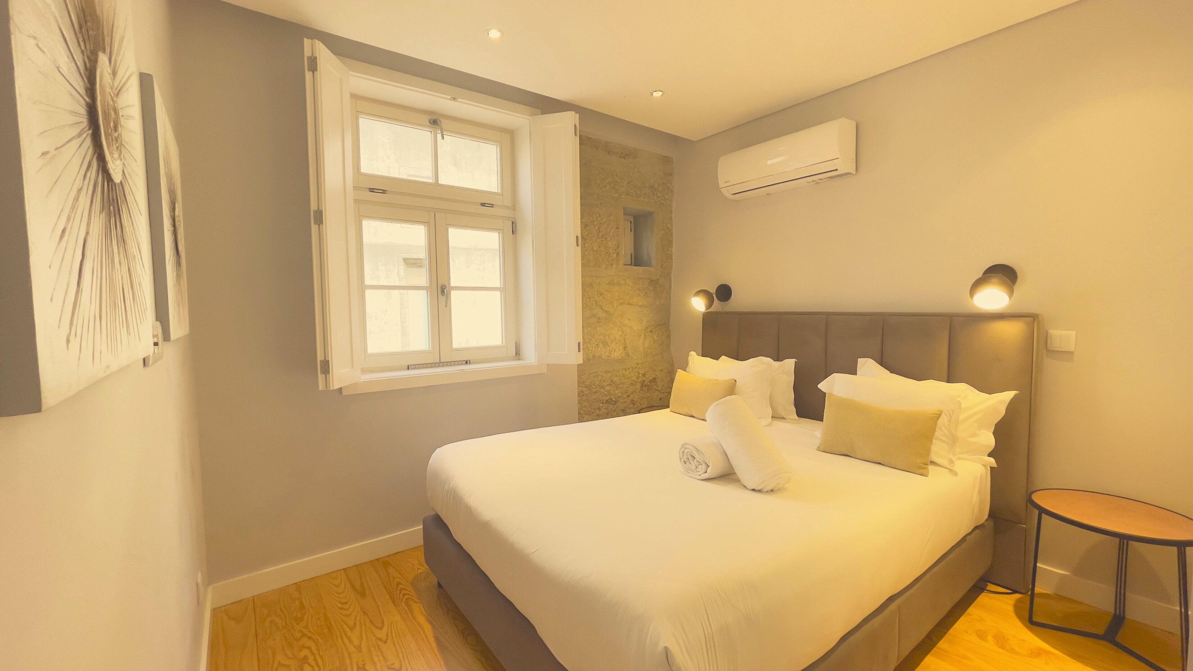 Quarto com uma cama grande, janela, ar condicionado e mesa de cabeceira.