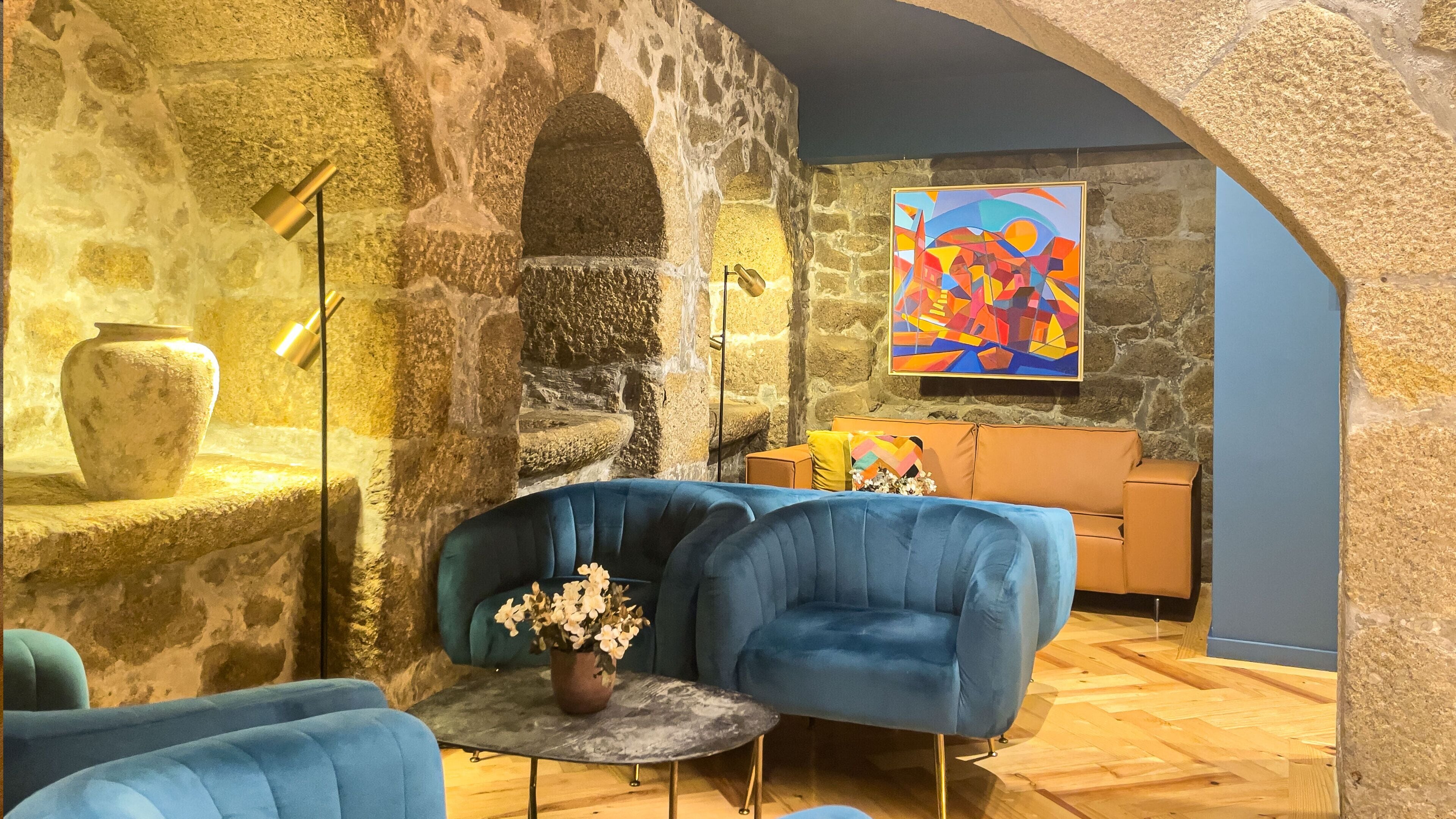 Una stanza accogliente con pareti in pietra, un divano blu, un tavolino con un vaso e un quadro colorato.