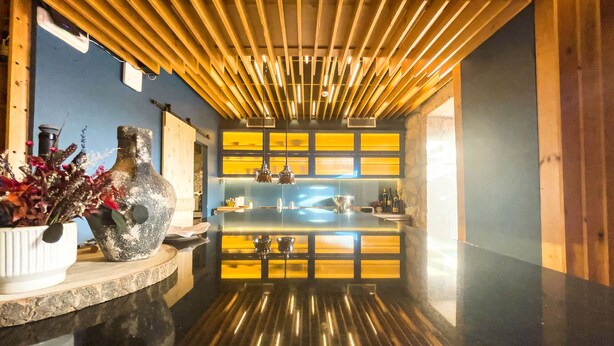 Una cucina moderna con isola centrale, travi in legno al soffitto e una parete blu con pannelli gialli.