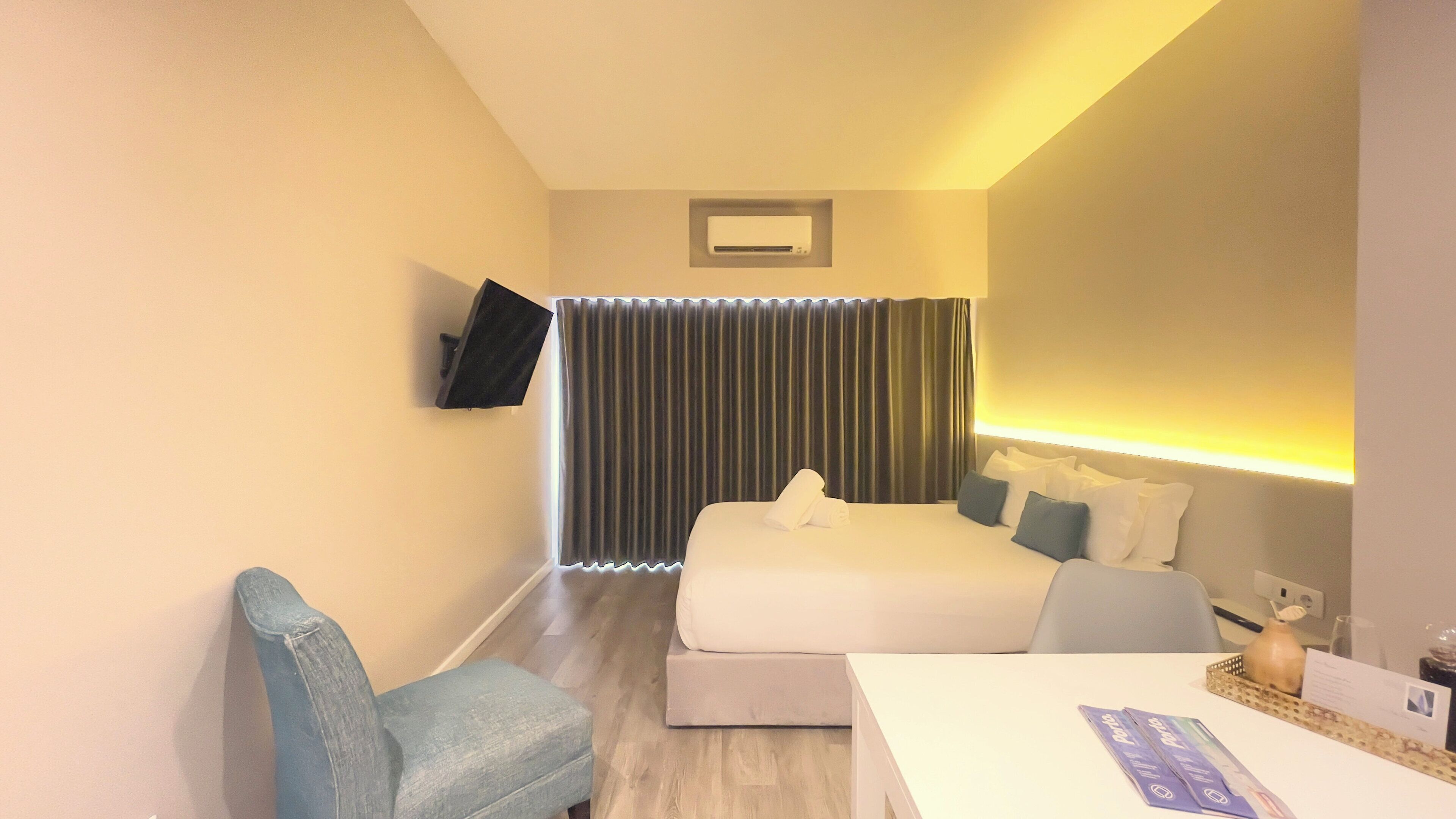 Habitación de hotel con cama, escritorio, silla, televisor montado en la pared y ventana con cortinas.