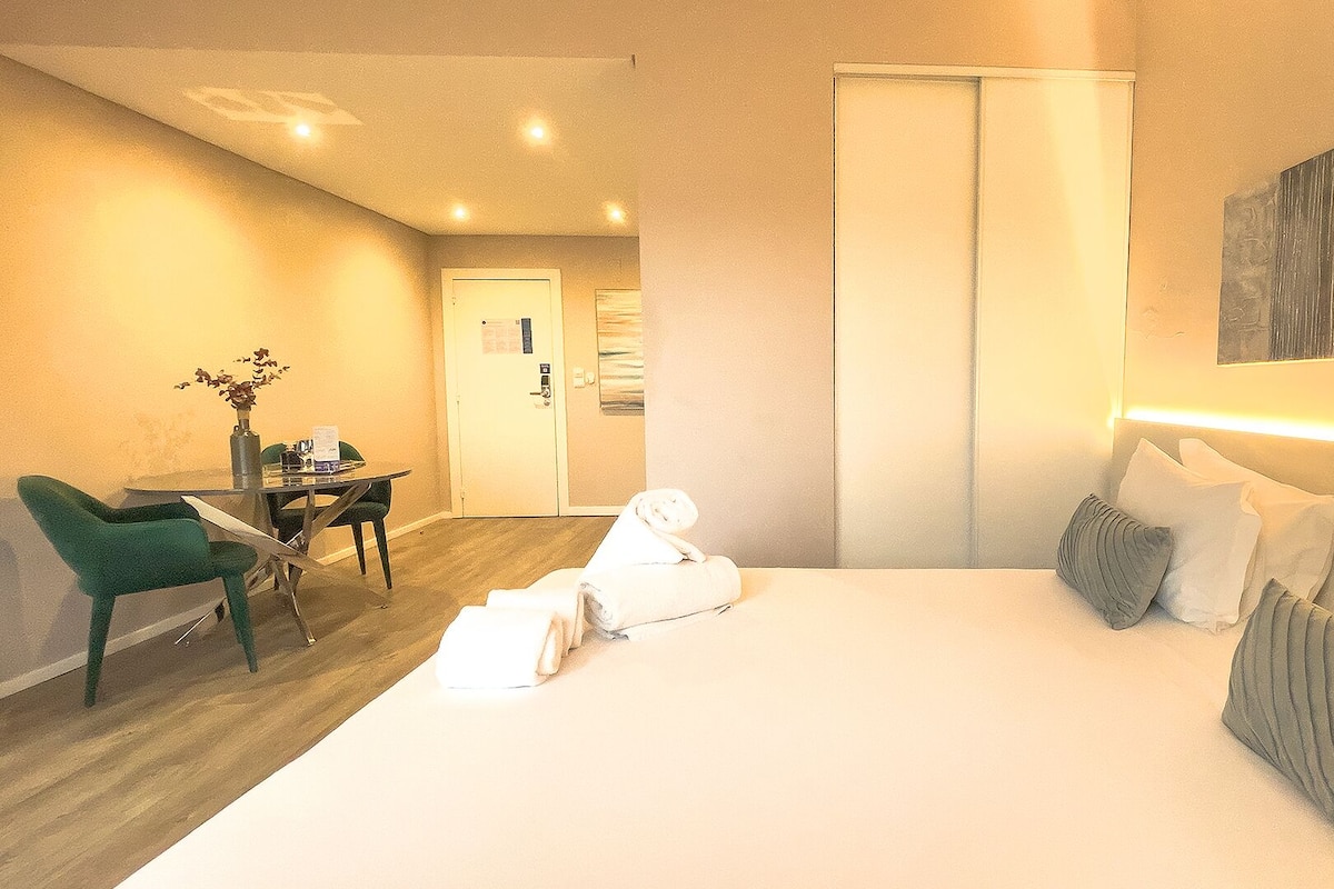 A hotel room with a bed, a desk, a chair, and a painting on the wall.