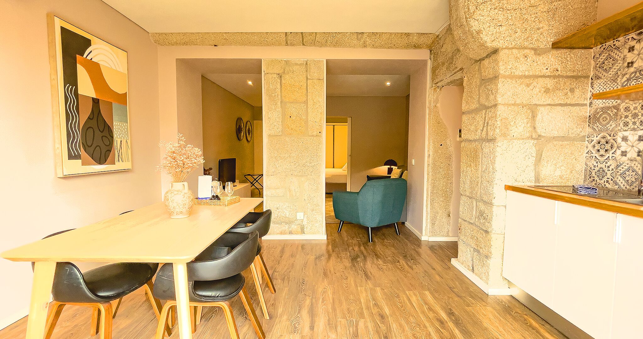 Un comedor con mesa y sillas de madera, un jarrón con flores secas y una pared de piedra.