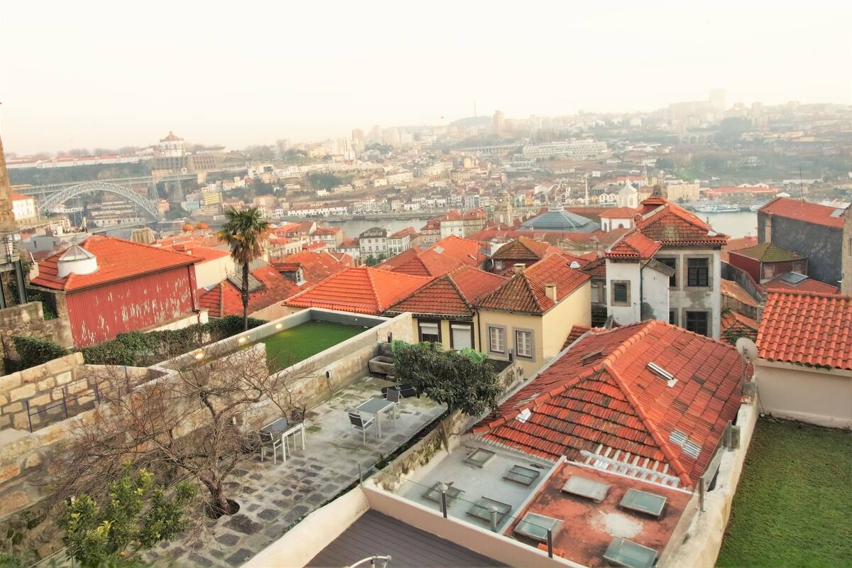 A residential area with red-tiled roofs, a view of a bridge, and a river in the background.