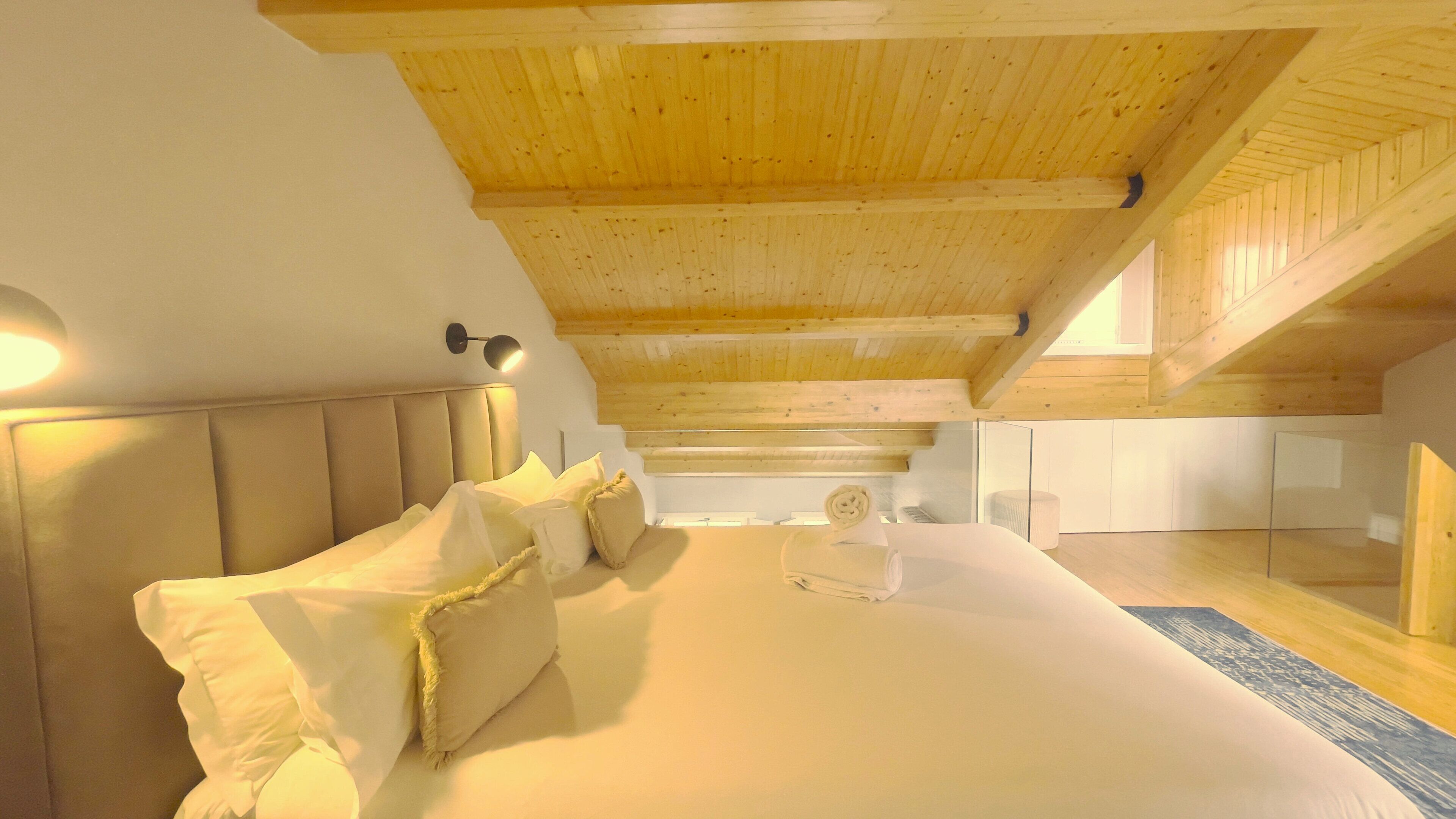 Ein Schlafzimmer mit Holzbalkendecke, einem Bett mit weißer Bettwäsche und einem Kopfteil.