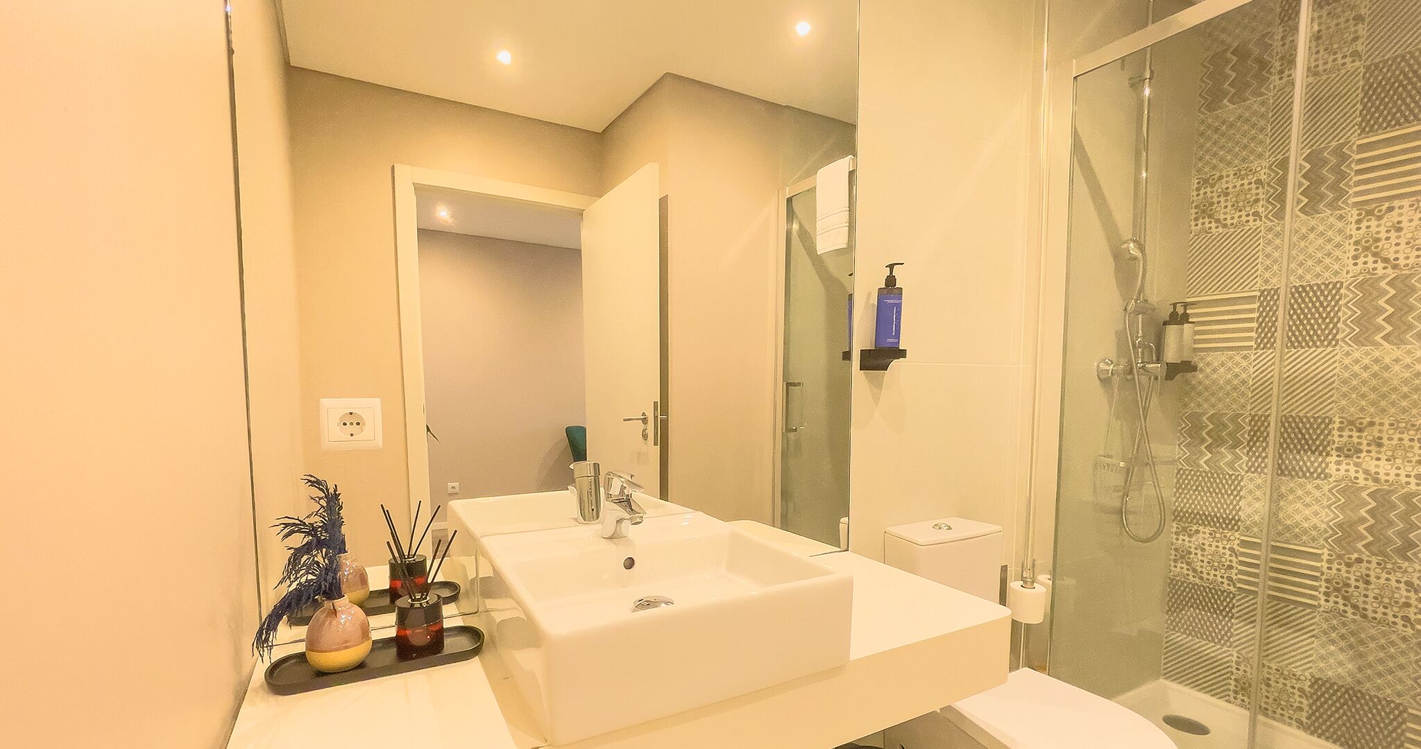 Ein modernes Badezimmer mit einem großen Waschbecken, einer Duschkabine aus Glas und einem Spiegel.