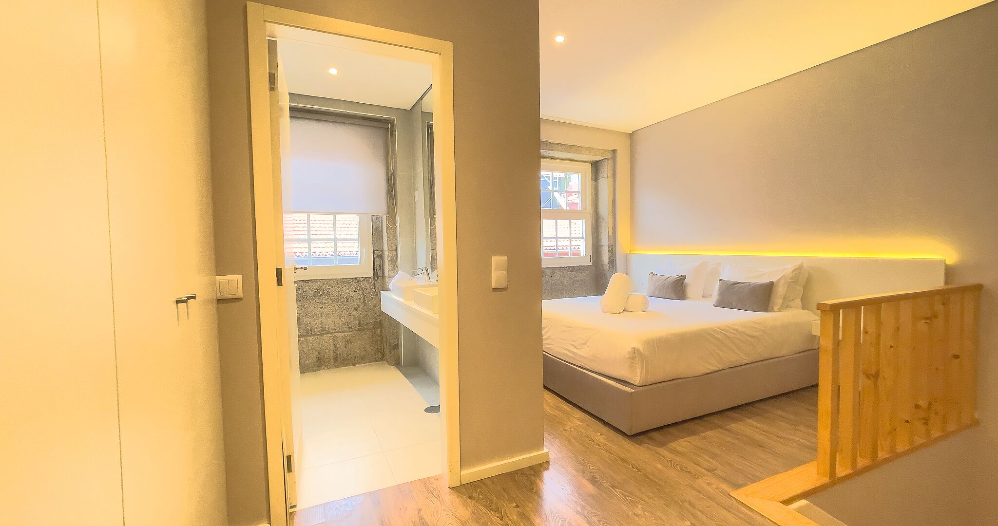 A bedroom with a bed, a wooden headboard, a bathroom with a sink and mirror, and a window.