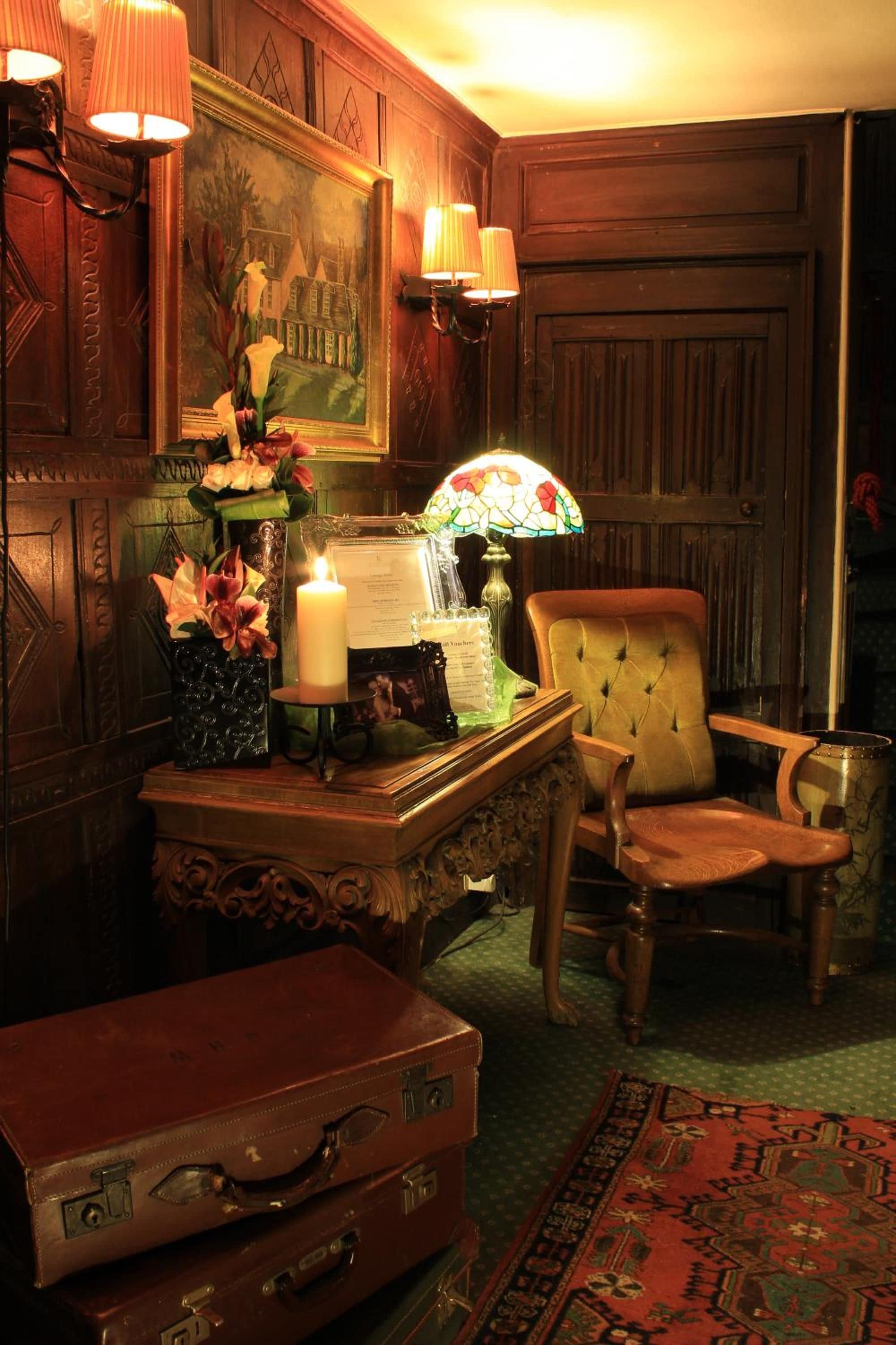 A room with a wooden cabinet, a chair, a table with a candle, a lamp, and a rug.