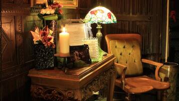 A room with a wooden cabinet, a chair, a table with a candle, a lamp, and a rug.