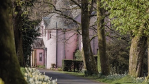 A pink building with a tower, surrounded by trees and a pathway.