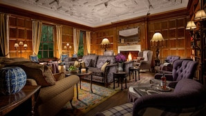 A traditional room with a fireplace, patterned sofas, and a bookshelf.