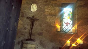 A stone-walled interior with a wooden door, a stained glass window, a crucifix, and a star-shaped light fixture.