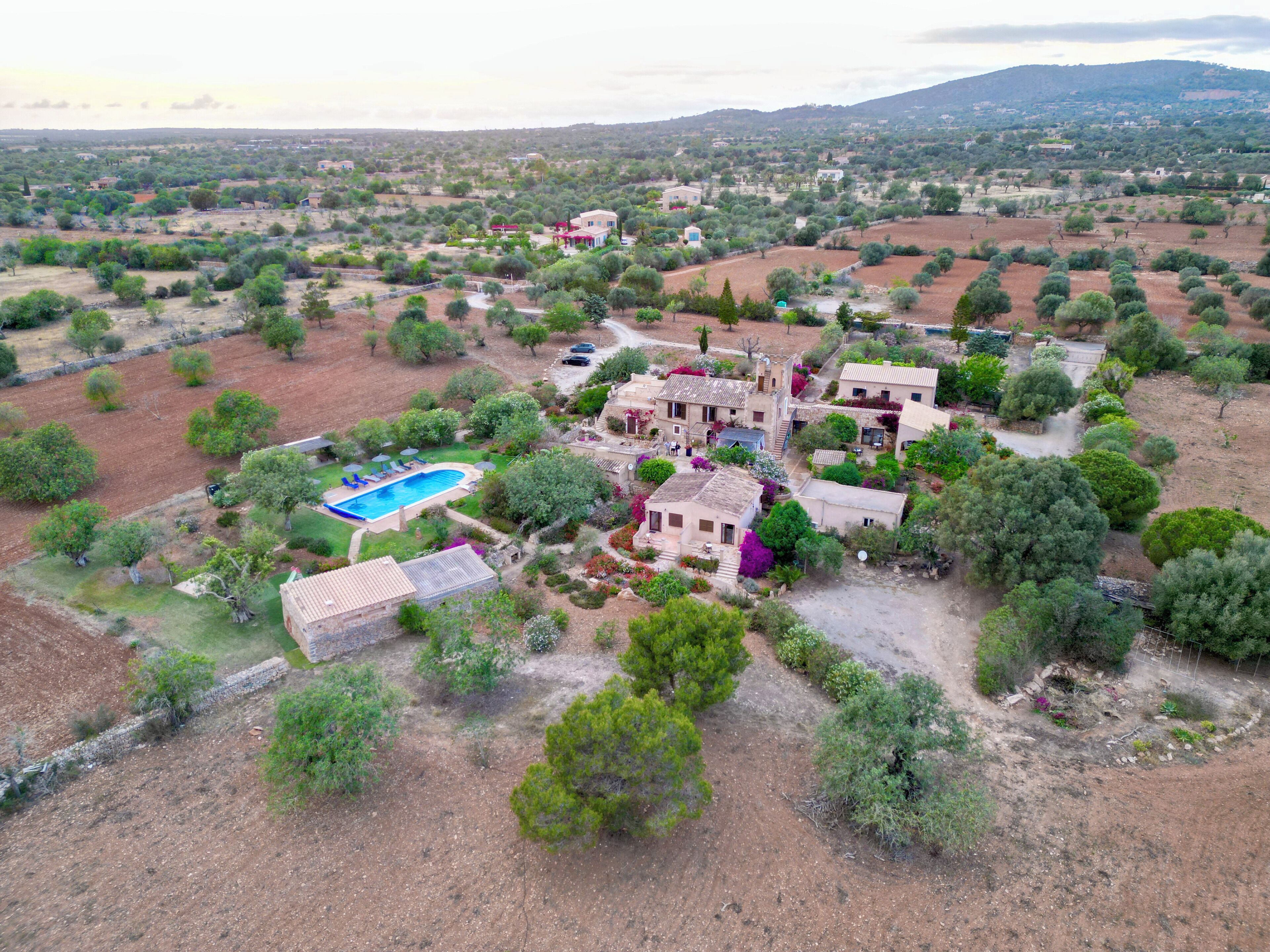 An aerial view of a rural property with a swimming pool, multiple buildings, and surrounding vegetation.