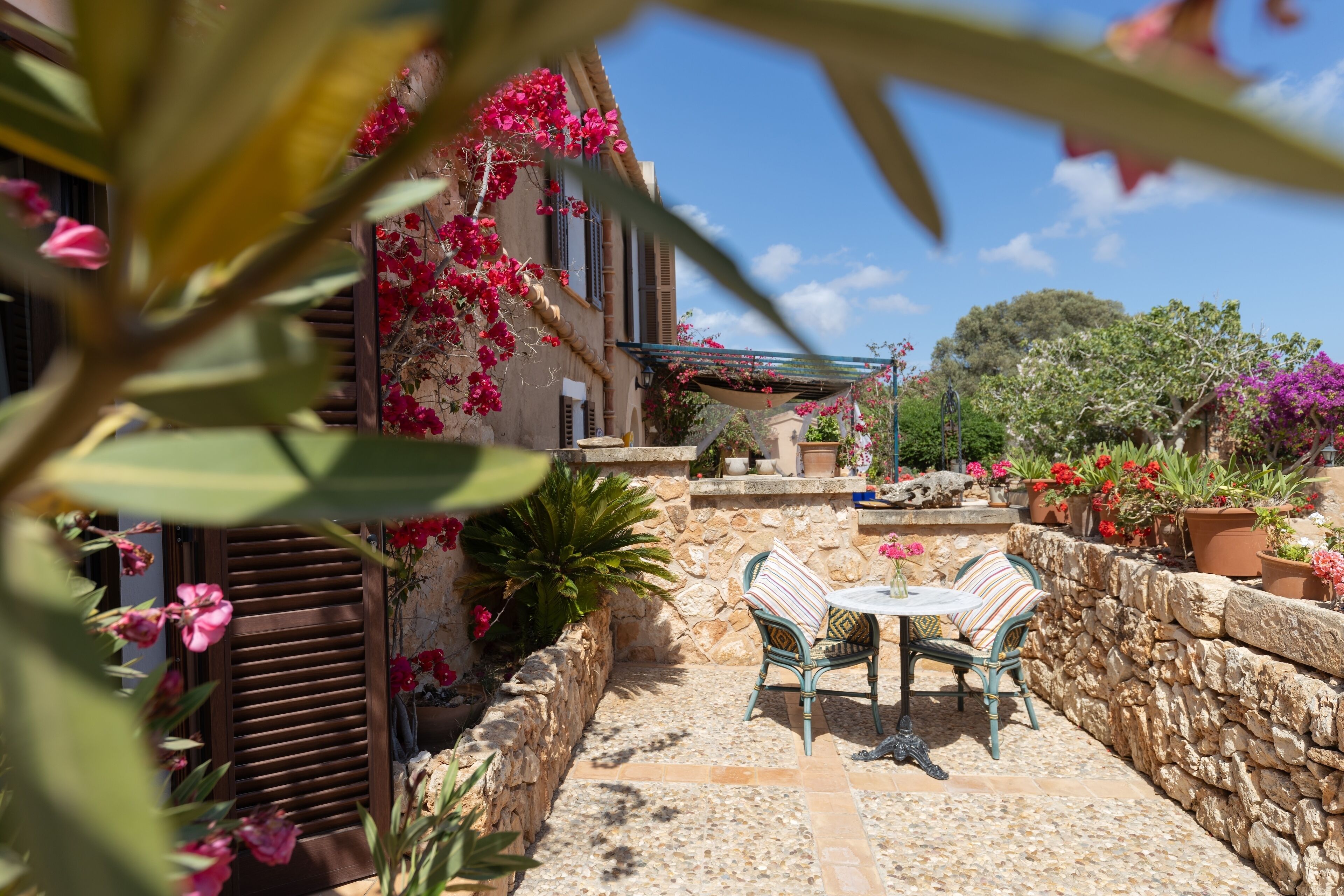An outdoor patio with stone flooring, two wicker chairs, a small table, and a stone wall.