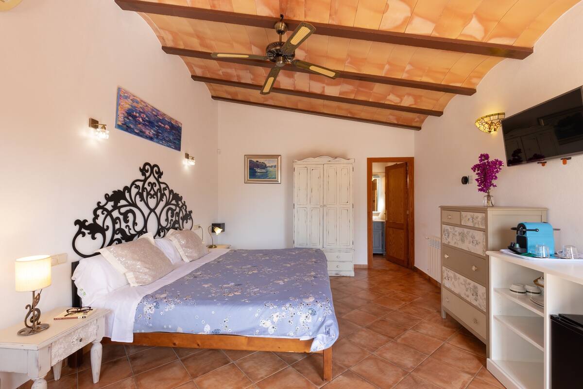 A bedroom with a bed, a nightstand, a wardrobe, a ceiling fan, and a television.