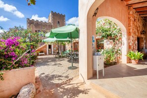 An outdoor patio area with tables and chairs, a stone wall, and a view of a castle-like building in the background. - Finca Son Marimon - Adults Only (Santanyi)