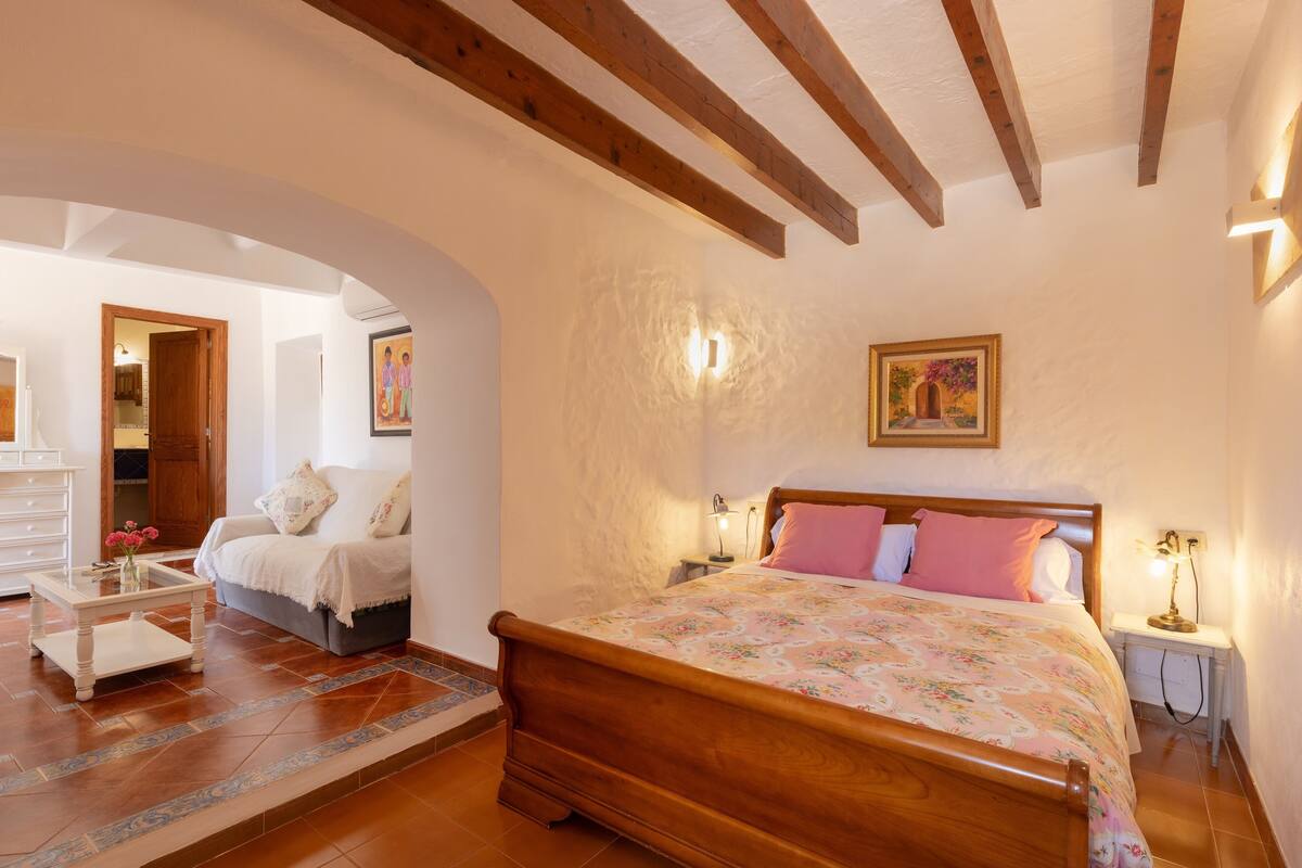 A bedroom with a wooden bed, a nightstand, a bedside table, and a painting on the wall.