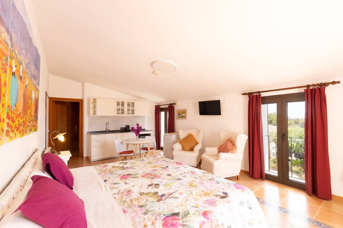 A bedroom with a bed, a desk, a chair, and a balcony with curtains.