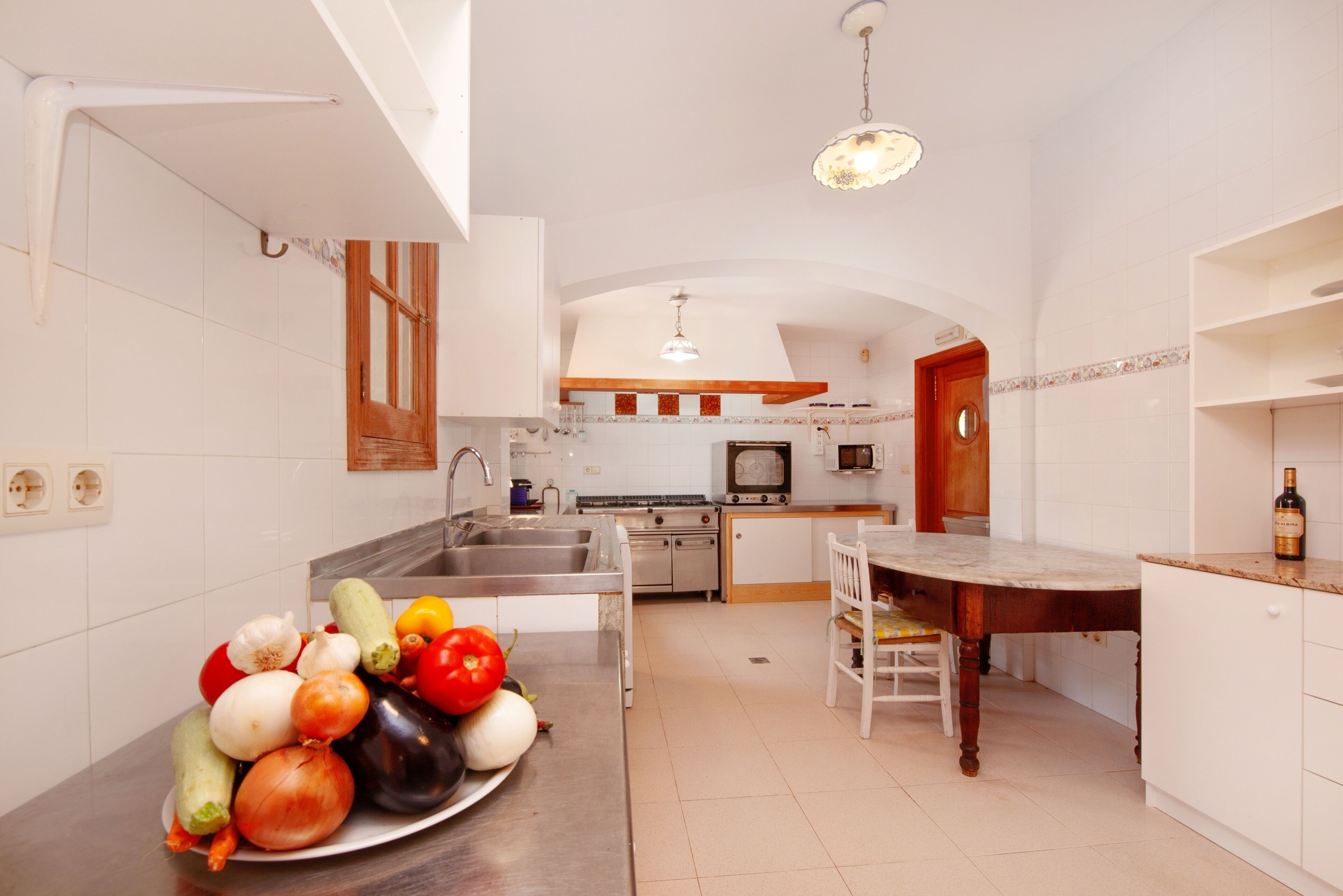Una cocina con armarios blancos, una mesa de comedor de madera y una variedad de verduras sobre la encimera.