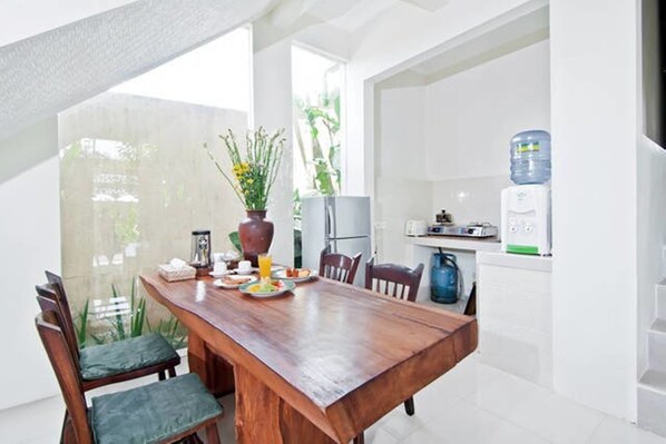 A dining area with a wooden table and chairs, a potted plant, and a water dispenser.