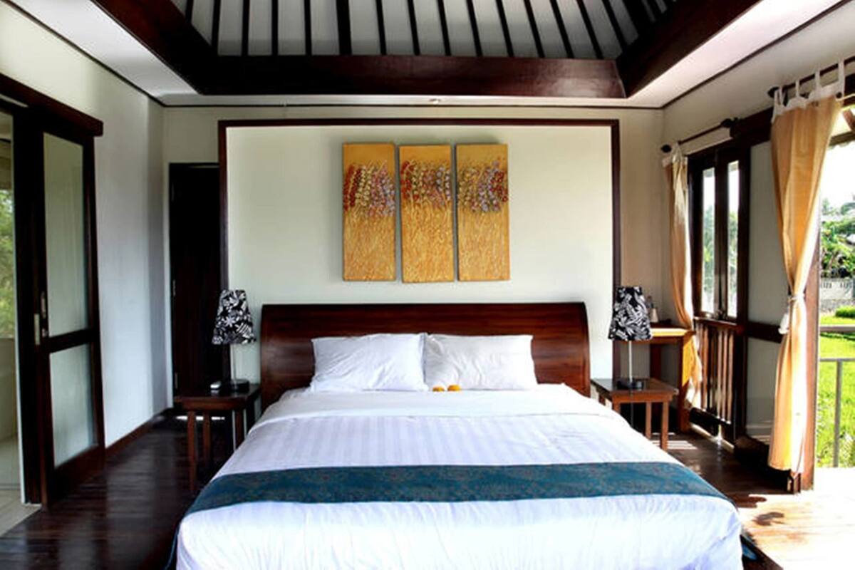 A large bed with a wooden headboard, two bedside tables, and a view of a garden through a window.