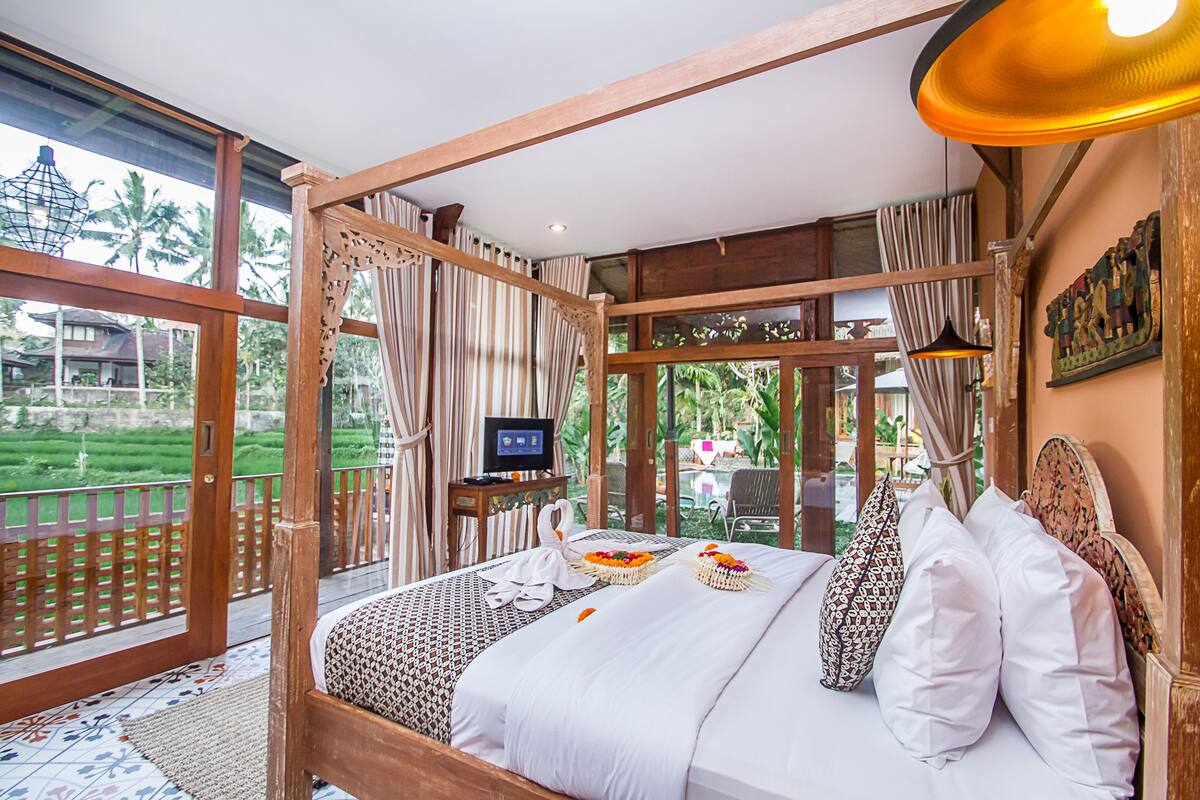 A spacious bedroom with a large bed, a television, and a view of a lush garden.
