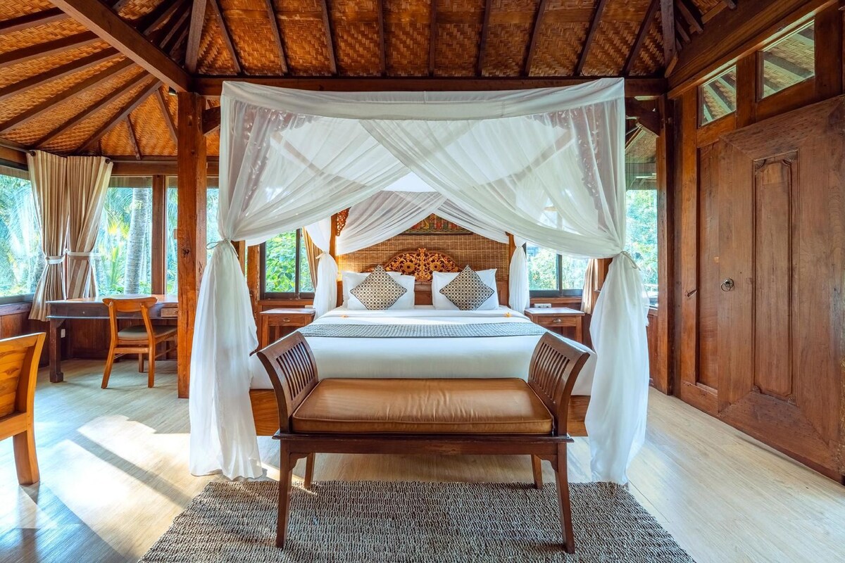 A bedroom with a canopy bed, a desk, and a view of the outdoors.