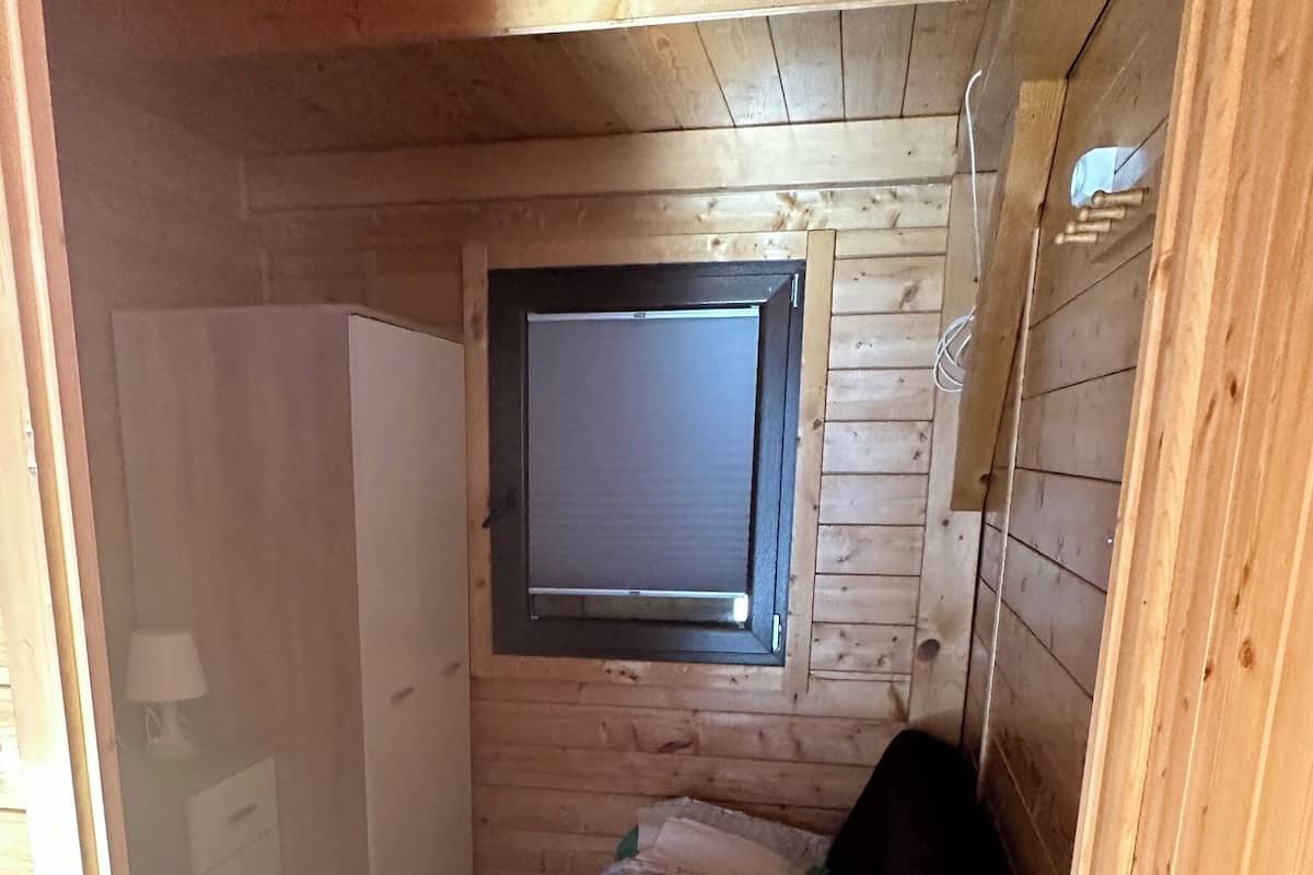 Quarto compacto com cama, janela e porta.