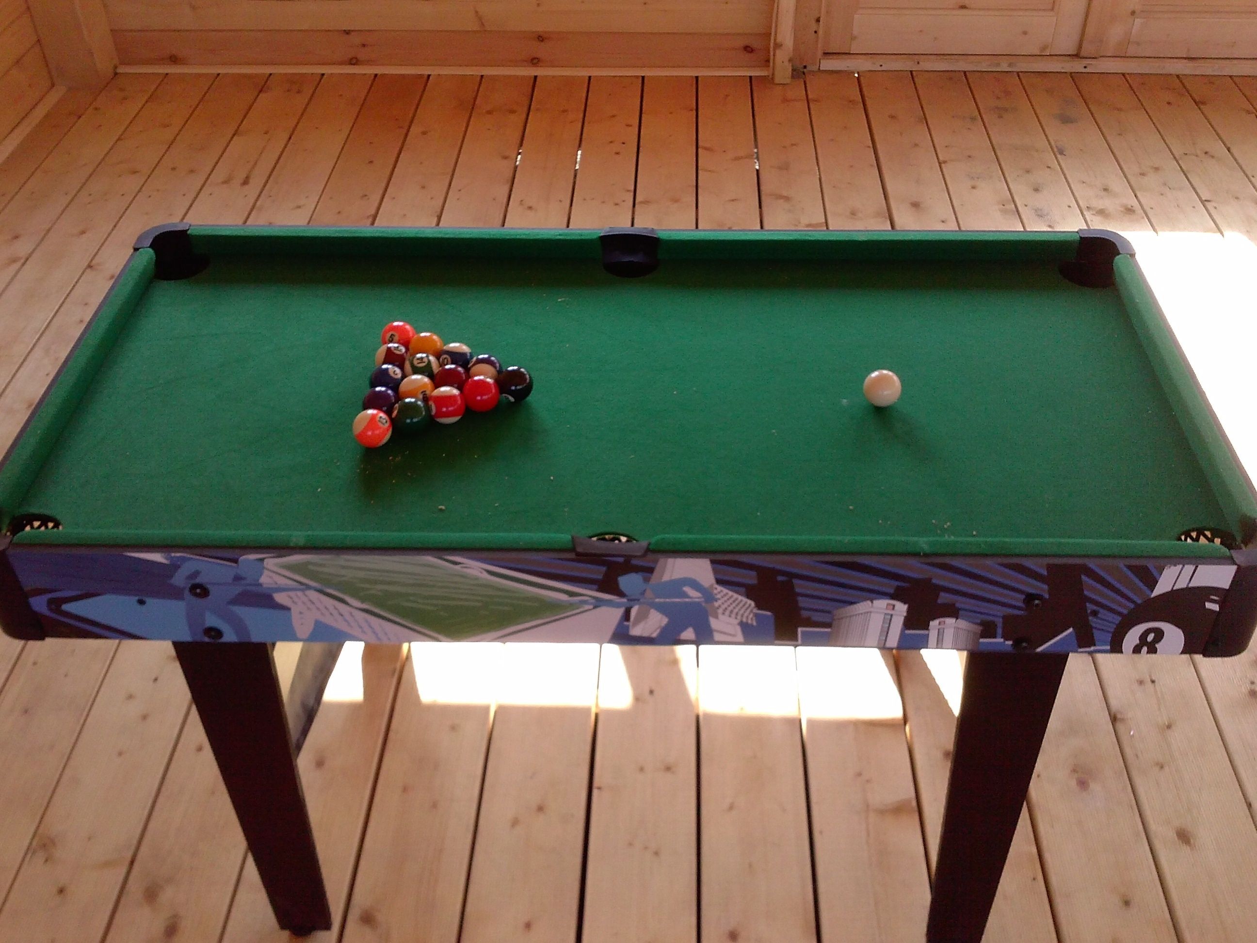 A pool table with a green felt surface, a triangular arrangement of billiard balls, and a single white cue ball.