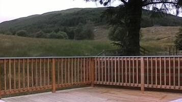 Una terraza de madera con vistas a un campo verde y colinas al fondo.