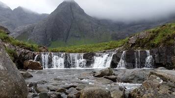 A waterfall cascading over rocks in a mountainous area with a prominent peak in the background.